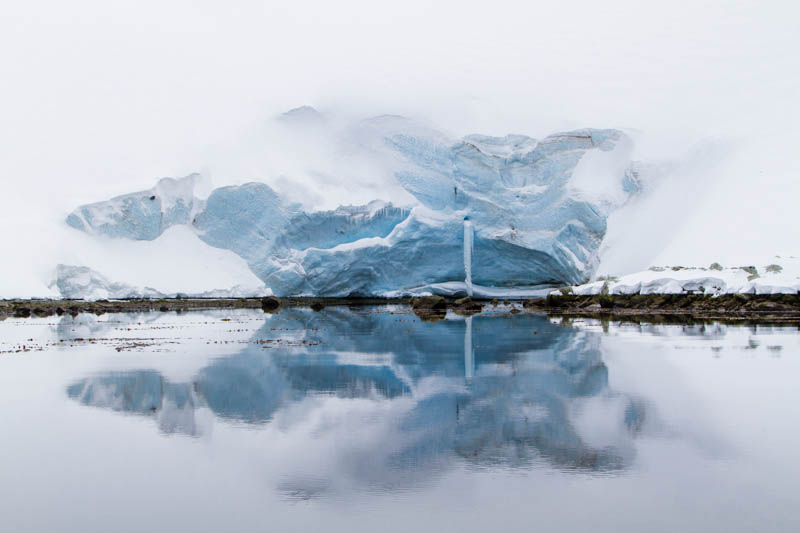 Ice Caves And Frozen Waterfall Reflected In Fjord